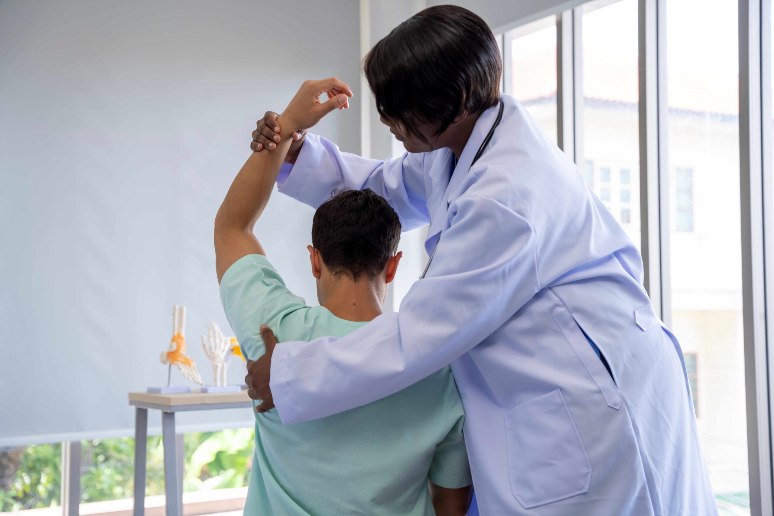 Optimizing Recovery: The Role of Rehabilitation Post-Orthopaedic Surgery A female doctor in a white coat assists a male patient in a physical therapy session, guiding his arm in an exercise to evaluate or improve joint mobility.