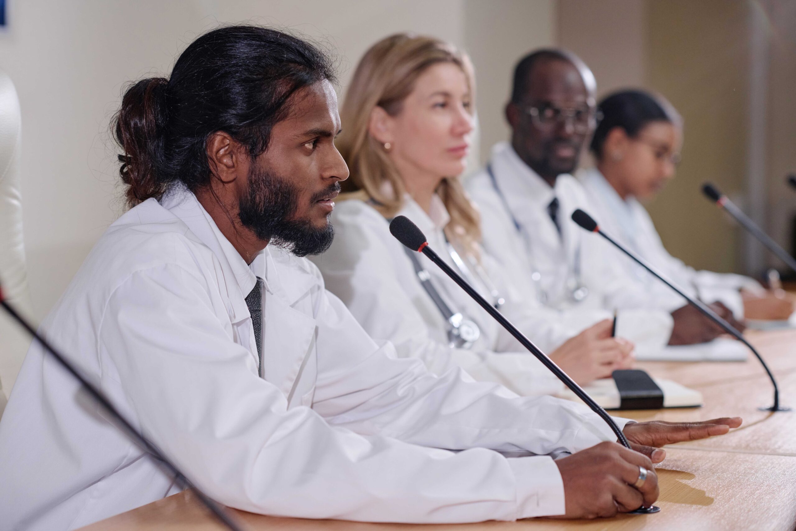 Navigating Disparities in Orthopaedic Care: A Call to Action A diverse panel of medical professionals in white coats is seated at a conference table, engaging in a panel discussion or press conference.