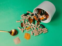 The Role of Nutritional Supplements in Bone Healing and Joint Health in Orthopaedics A white container tipped over on a green tabletop, spilling various capsules and supplements, with a golden spoon and powders beside it.