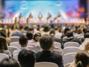 Upcoming Orthopaedic Summit! An audience seated and attentively listening to speakers on stage during a conference or seminar.