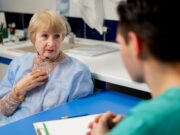The Importance of Patient-Reported Outcome Measures (PROMs) in Joint Replacement An elderly woman in a hospital gown is having a consultation with a healthcare professional in a clinical setting.