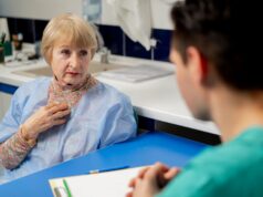 The Importance of Patient-Reported Outcome Measures (PROMs) in Joint Replacement An elderly woman in a hospital gown is having a consultation with a healthcare professional in a clinical setting.