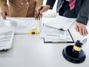 Legal Settlements Highlight Issues in Spine Care Two business professionals review legal documents and contracts at a desk with a gavel nearby.