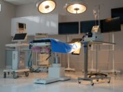 Impact of Technological Advancements on Total Hip and Knee Arthroplasty A modern, well-equipped operating room with surgical lights, an operating table covered in blue drapes, and various medical monitors and equipment.