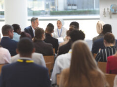 Annual AOSSM Meeting 2024: Reaching New Heights in Sports Medicine A diverse group of business professionals attentively listens to a panel discussion in a bright, modern conference room.