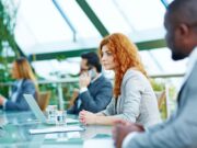 Revitalize Orthopaedic Care: Join Orthopaedics 2024 in Paris! A young woman attentively listens during a business conference, surrounded by colleagues in a modern setting.