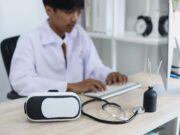 Expert Predictions: The Future Landscape of Orthopaedic Surgery A doctor in a white coat works at a computer, with a virtual reality headset and a stethoscope on the desk beside him.